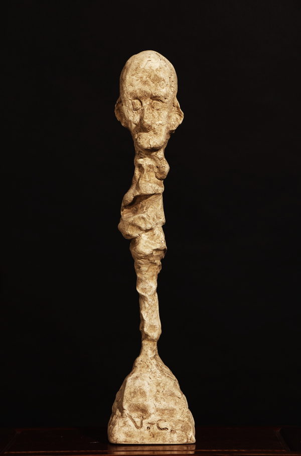 The Contemplative One (2023) by Valeriu Cazacevschi. An ochre-coloured elongated head on a textured narrow stem and foot.