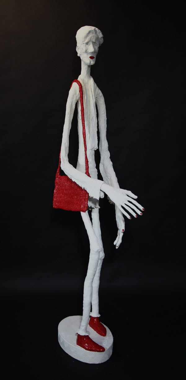 A slender pale figure with a red shoulder bag, red shoes and extended hands.