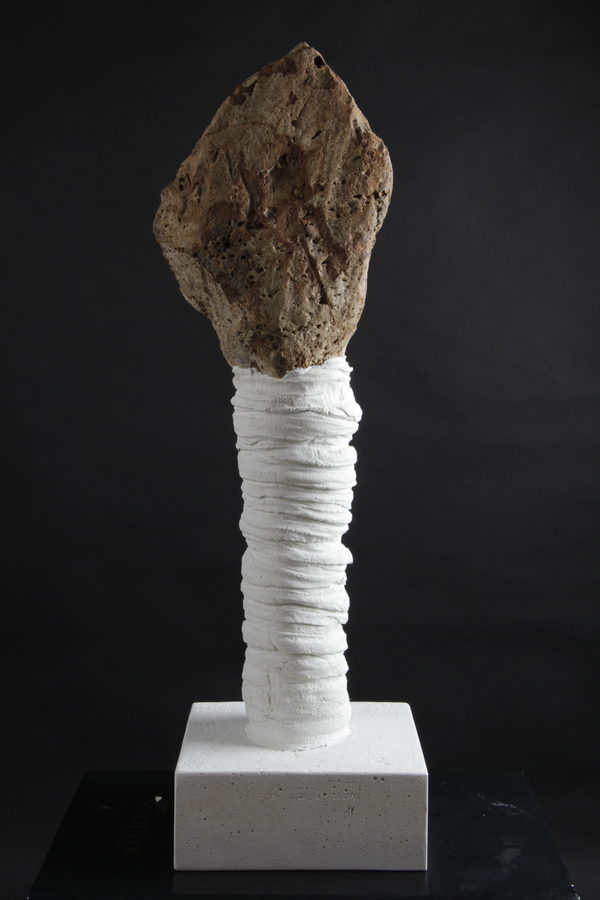 Frontal view of the rough, irregular upper form above the white wrapped column and square pale base.
