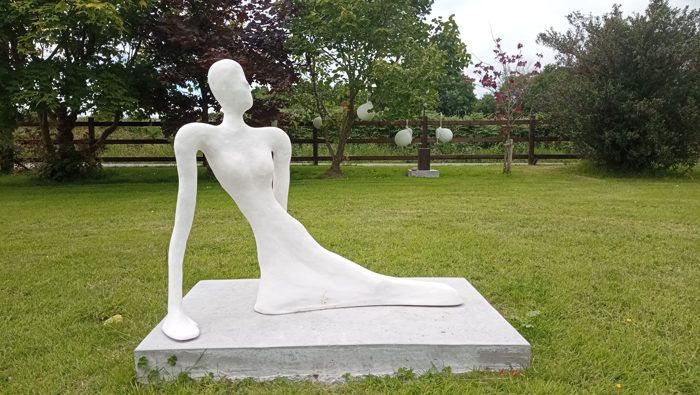 White reclining figurative sculpture on a rectangular base outdoors
